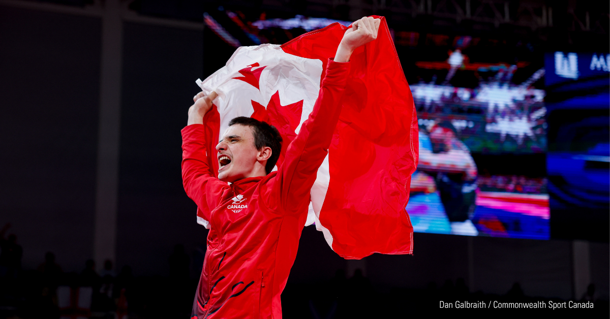 Jordan Carroll celebrates with a large Canadian flag held aloft, wearing a red outfit with "Canada" visible on it.